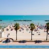 Spiaggia affollata con palme e mare.