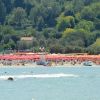 Spiaggia con numerosi ombrelloni rossi e verde vegetazione alle spalle.