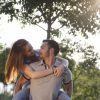 Coppia giovane, la donna sulla schiena dell'uomo, in un parco con alberi verdi.