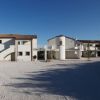 Un edificio modernista bianco su un ampio cortile di ghiaia, con cielo azzurro sopra.