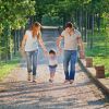 Due adulti e un bambino camminano felici in un viale alberato, tenendosi per mano.