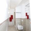 Un bagno moderno con piastrelle beige, asciugamani rossi e servizi igienici.