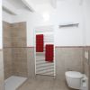 Un bagno con piastrelle beige, doccia aperta, scaldasalviette bianco e asciugamani rossi.