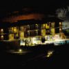 Edificio moderno illuminato di notte, con balconi e piscina, incorniciato da colline.