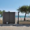 Spiaggia vista attraverso un cancello, con recinzione e alberi.
